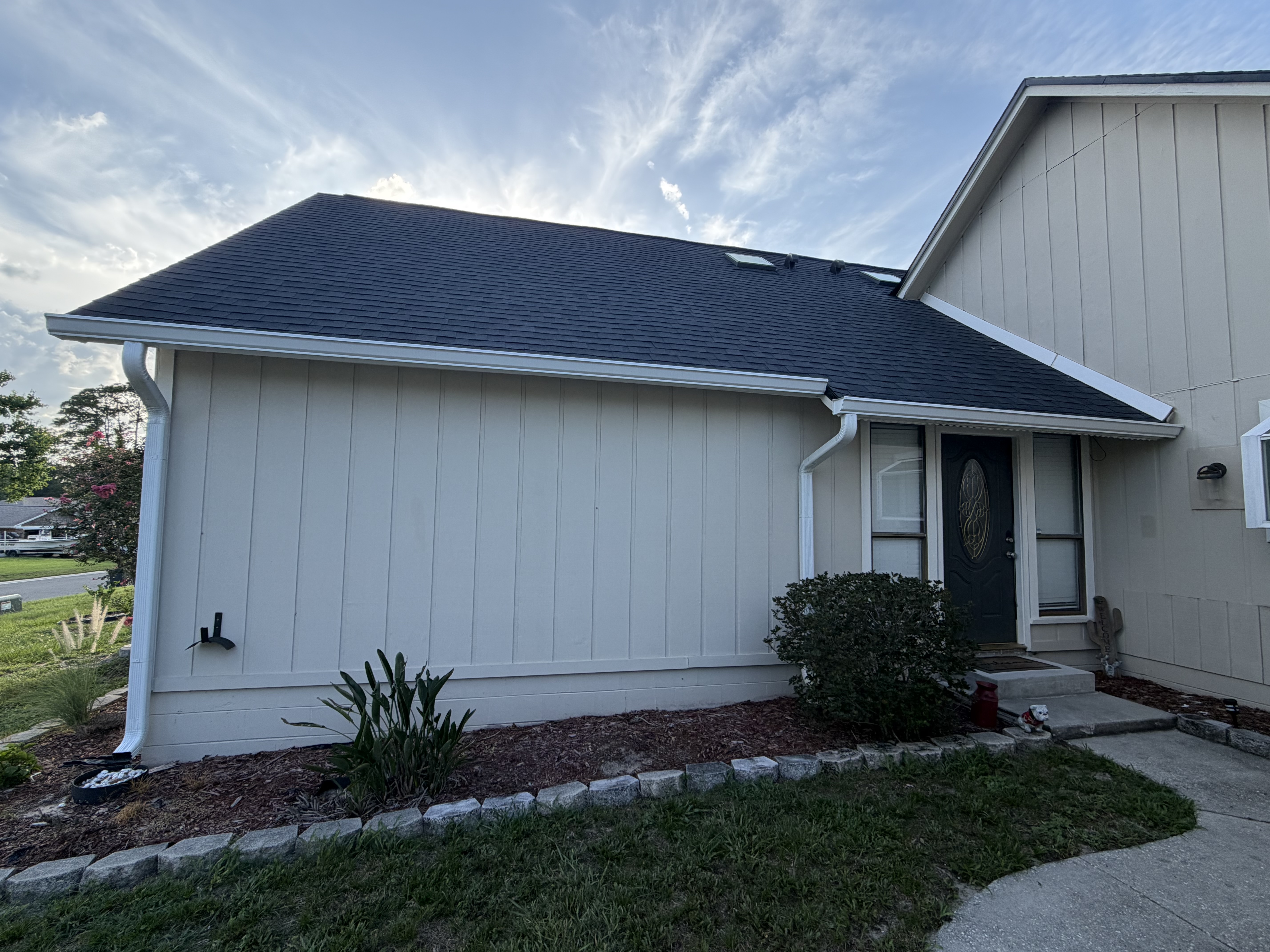 Tan siding ranch home rear exterior with new seamless gutters and shingle roof